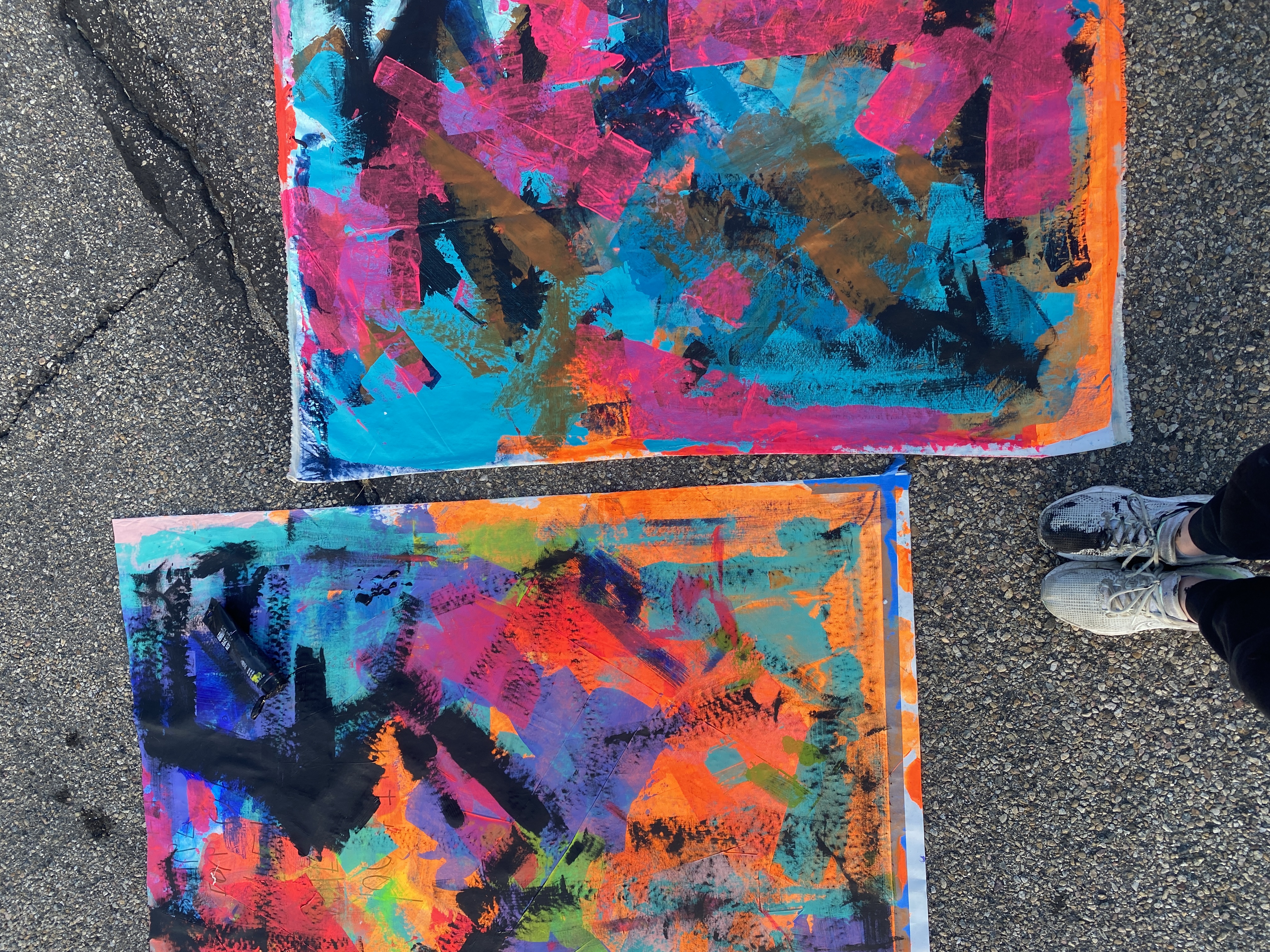 Two large vibrant abstract canvases drying on asphalt
